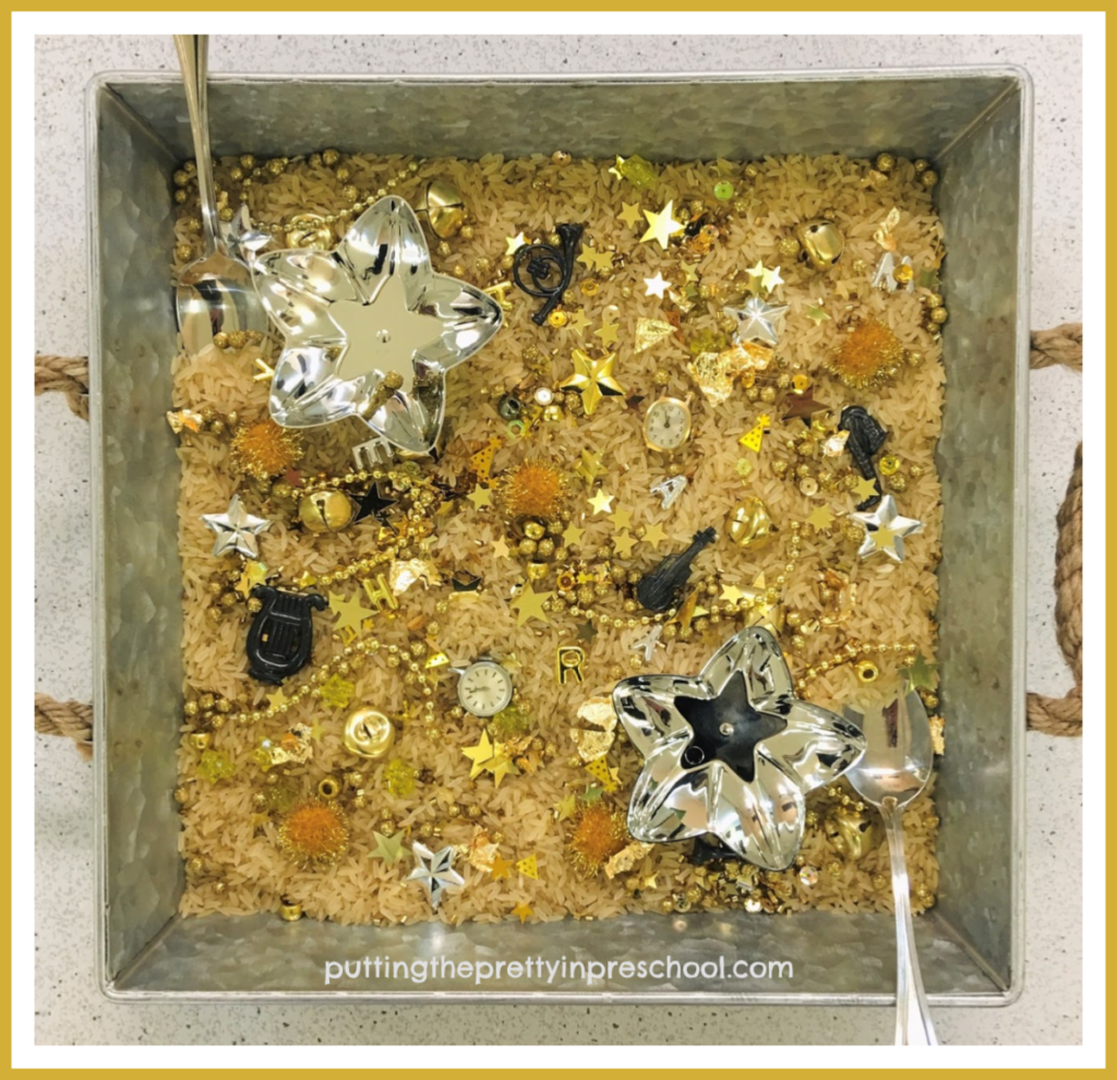 A square-shaped silver metal tray is perfect for showcasing the gold and silver pieces in this New Year's sensory play center.
