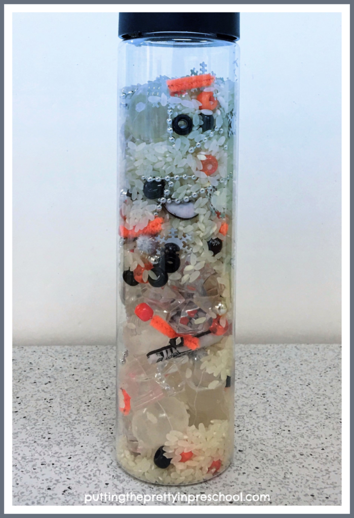 Snowman sensory tube with a rice base and loose parts. Snowman ice cubes and buttons are the highlights of the tube.