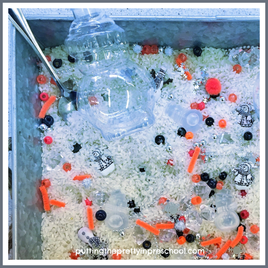 Snowman sensory tray with a rice base and loose parts. Snowman bottles, ice cubes, and buttons are the highlights of the tray.