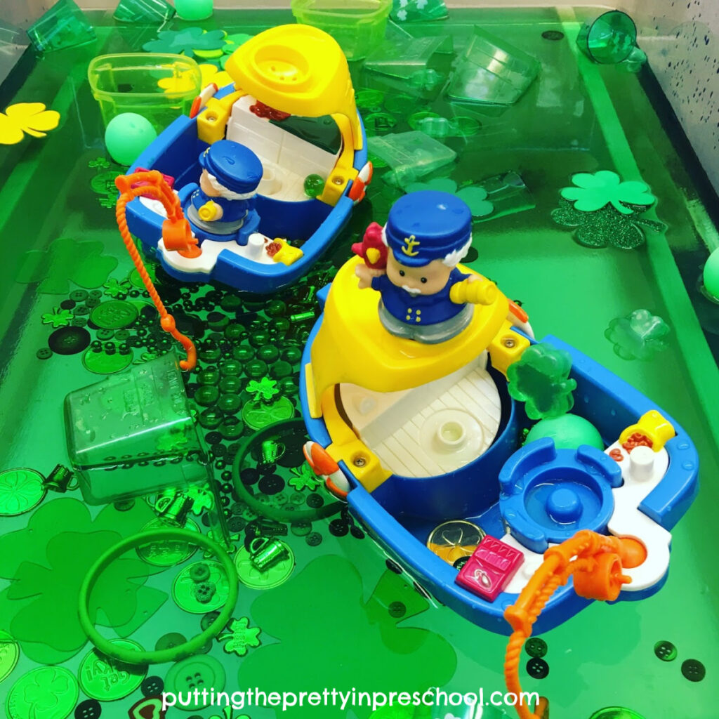 Toy boats on green water filled with St. Patrick's Day-themed loose parts offer a rich sensory play experience.