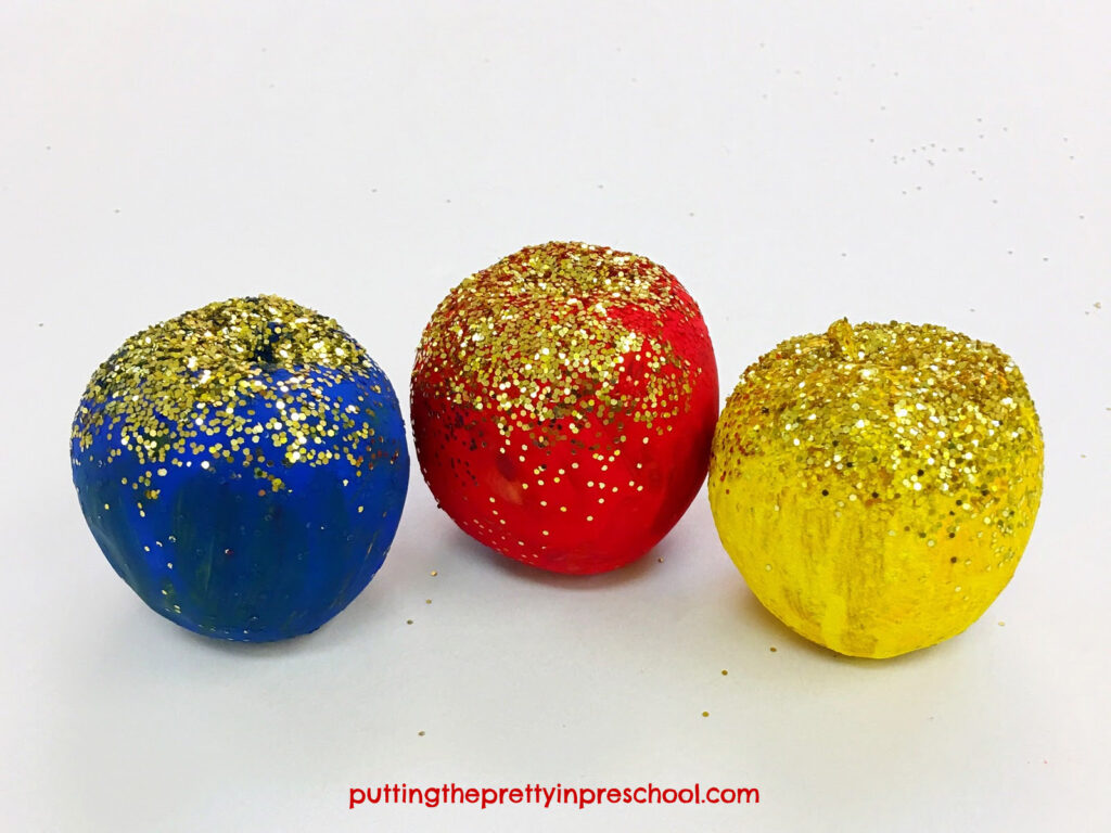 Apples painted in primary colors and sprinkled with glitter. This art activity is inspired by an apple painting by Auguste Rodin.