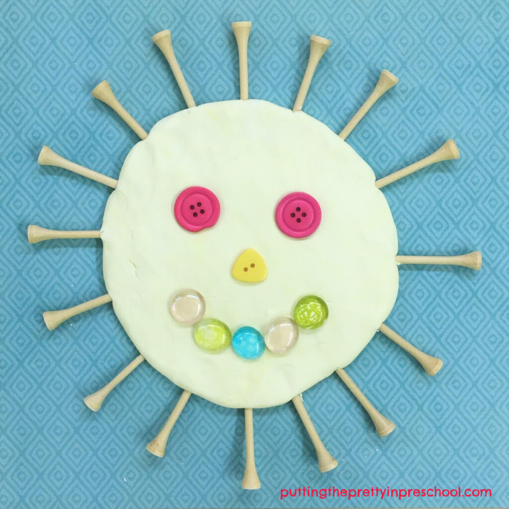 A playdough sun created with coconut-scented, two-ingredient playdough and buttons, gems, and golf tees.
