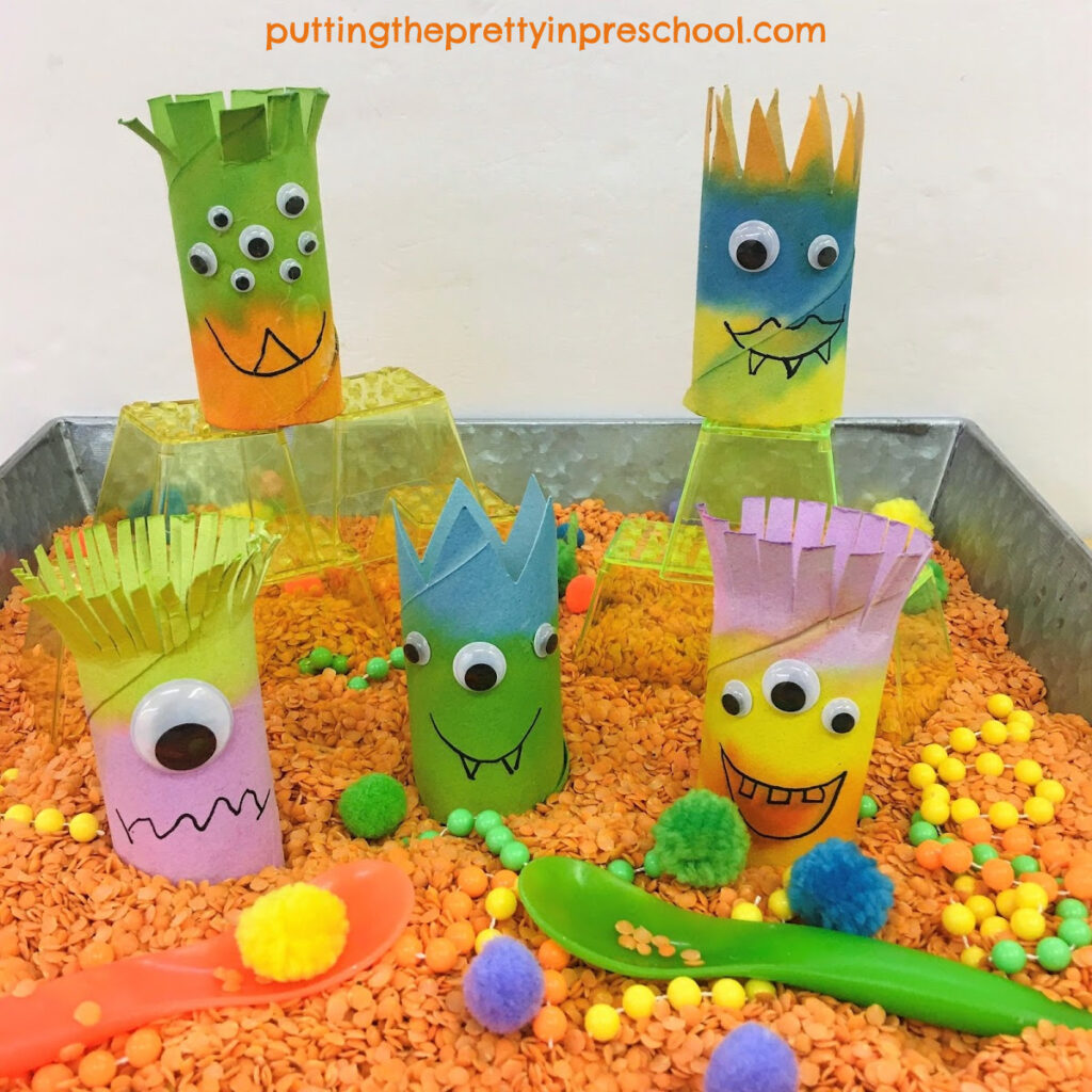 Toilet paper roll monsters in a red split lentil-based sensory bin perfect for imaginary play.