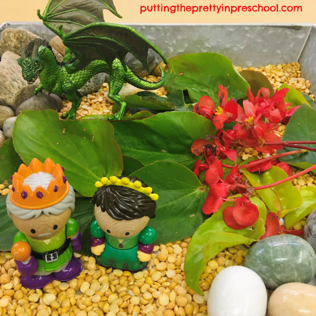 Castle-themed sensory bin with a dragon, king, princess, and dragon wing begonia leaves and flowers.