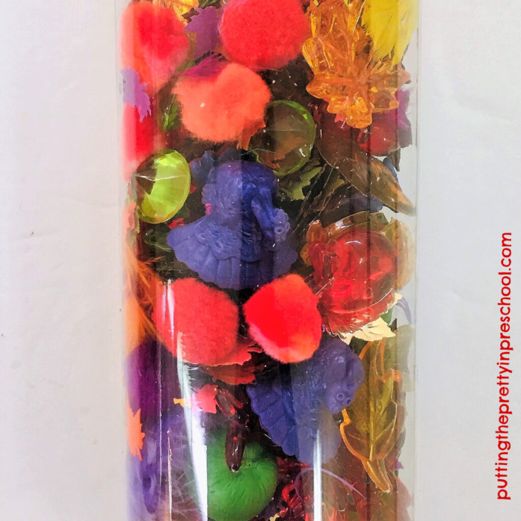 Glitter water sensory tube with turkey counters, and leaf, pumpkin, diamond, and apple gems.