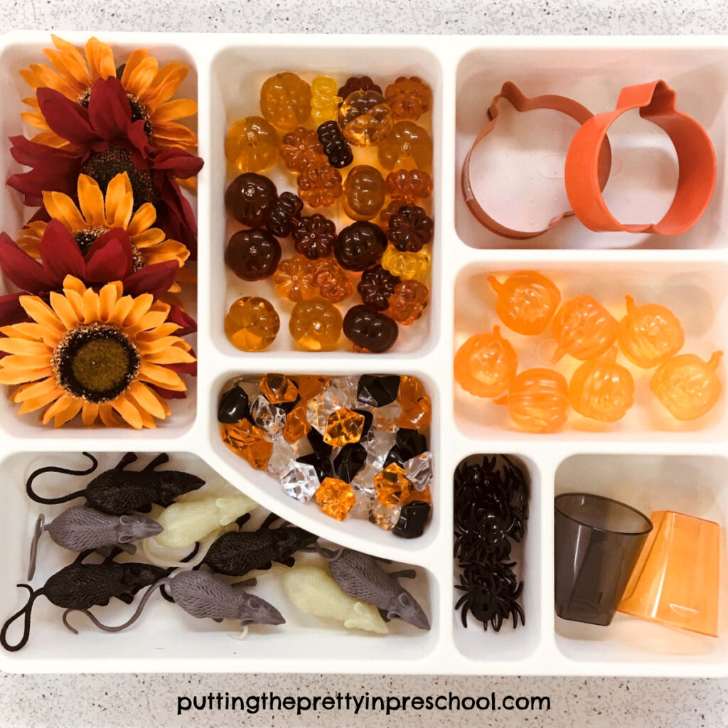 Fall-themed tinker tray with sunflowers, mice, spiders, gems, and pumpkin loose parts.