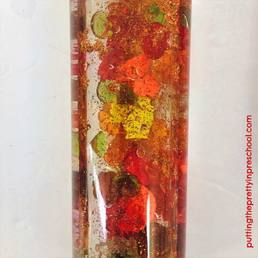 Glitter water sensory tube with turkey counters, and leaf, pumpkin, and apple gems.