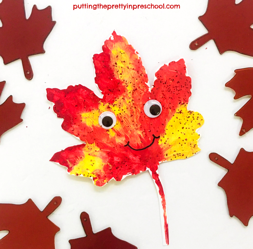 Crafted paint print maple leaf person with wiggly eyes and a permanent felt pen smile.