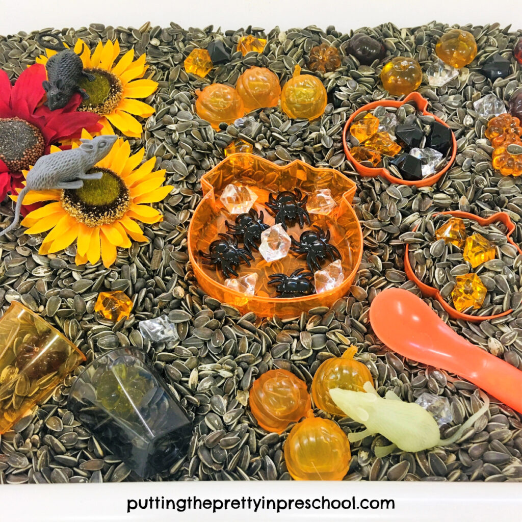 Pumpkin-themed loose parts and sunflowers shine in this sunflower seed sensory bin. Spiders and mice add fun to the tray.