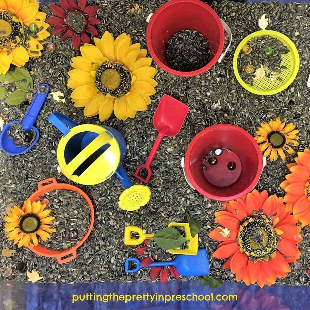 Sand toys, sunflowers, and fall-themed gems in a sunflower seed sensory bin.