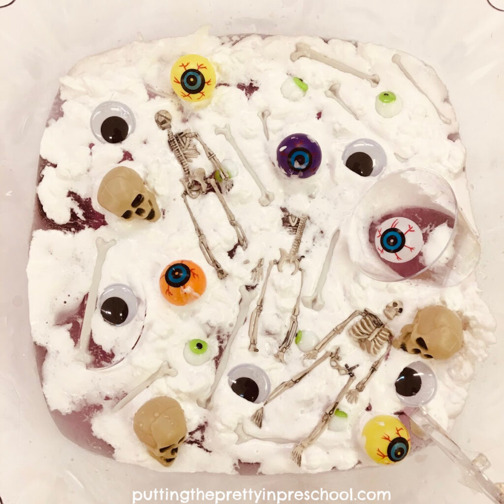 Eyeballs, wiggly eyes, skulls, bones, and skeletons float on shaving foam topped purple water in a tulip-shaped punch bowl.