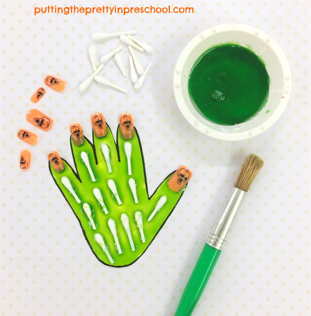 Green painted hand, decorated with Q-tip bones and orange skull-themed nails.