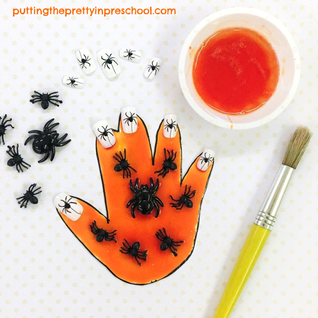 Orange painted hand, decorated with spiders and spider-themed nails.