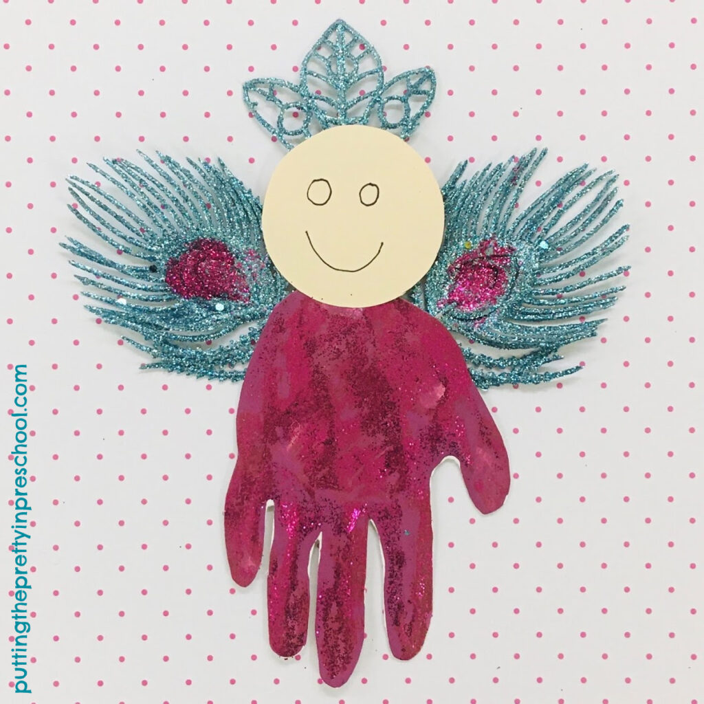 Christmas-themed handprint angel with glittery turquoise and magenta peacock-inspired wings.