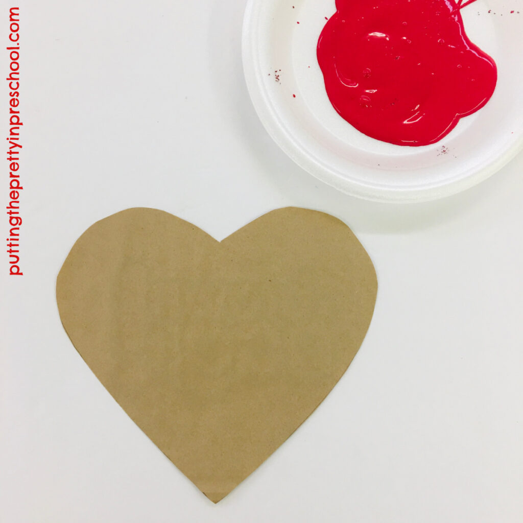 Invitation to make a red handprint on a paper bag heart.