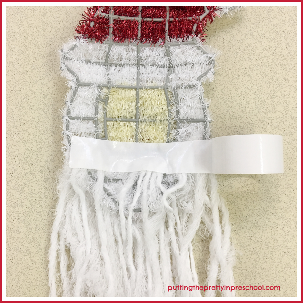 Back view of Santa Head Wall Decor. A strip of white duct tape stabilizes the threaded yarn beard extensions. A scissor activity for young children.
