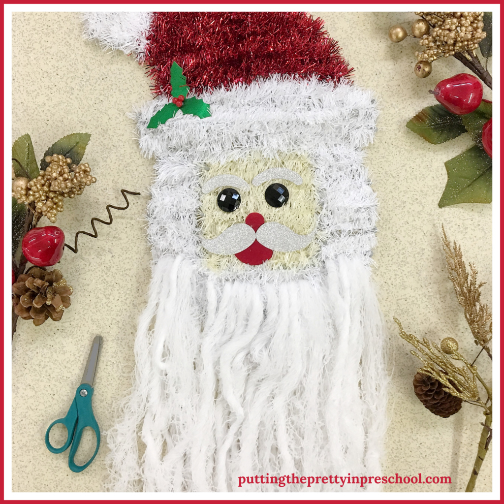 Santa head wall decor repurposed as a beard trimming scissor activity for young children. The white yarn is threaded through Santa's chin to add beard extensions perfect for cutting.