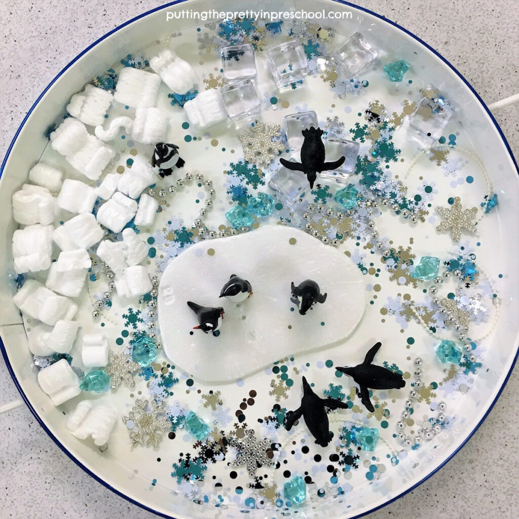 Penguin sensory tray with a snowflake confetti base.