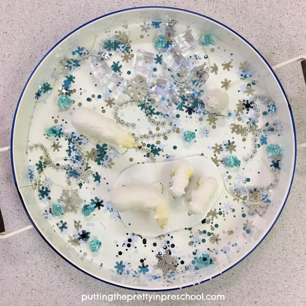 Polar sensory tray with a snowflake confetti base and shiny loose parts.