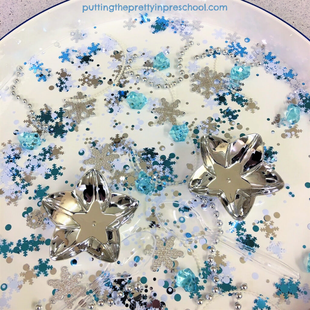 Snowflake studded winter sensory tray filled with shiny pieces.