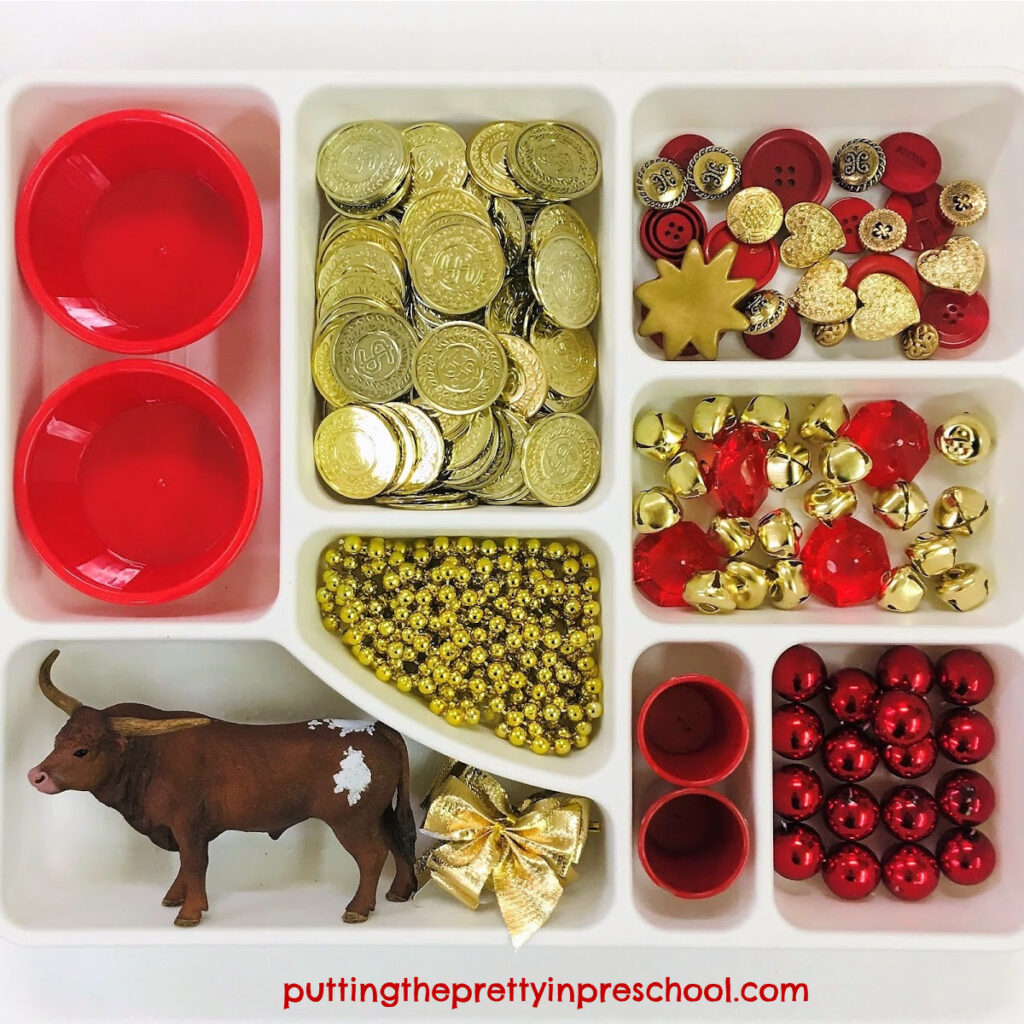 Chinese New Year loose parts tray featuring a bull figurine and red and gold loose parts.