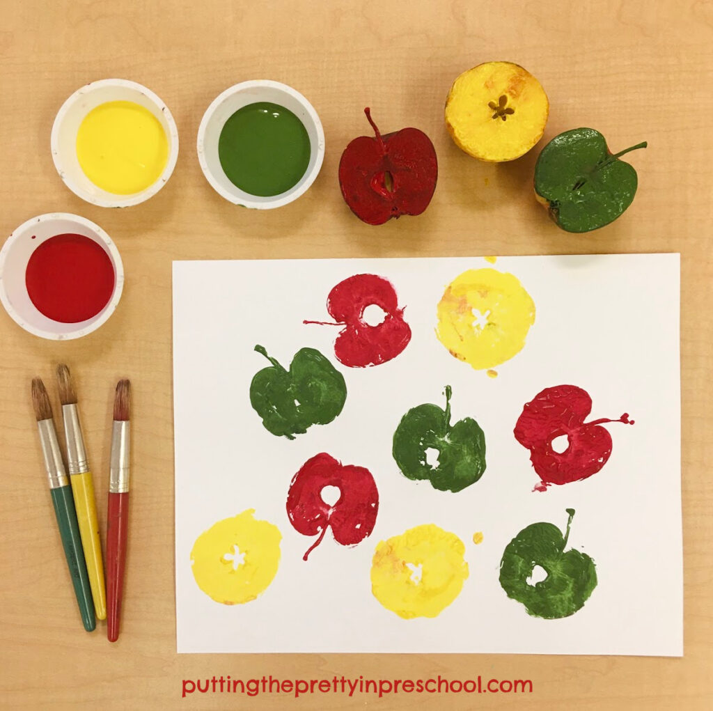 Apple printmaking with green, red, and yellow tempera paints.