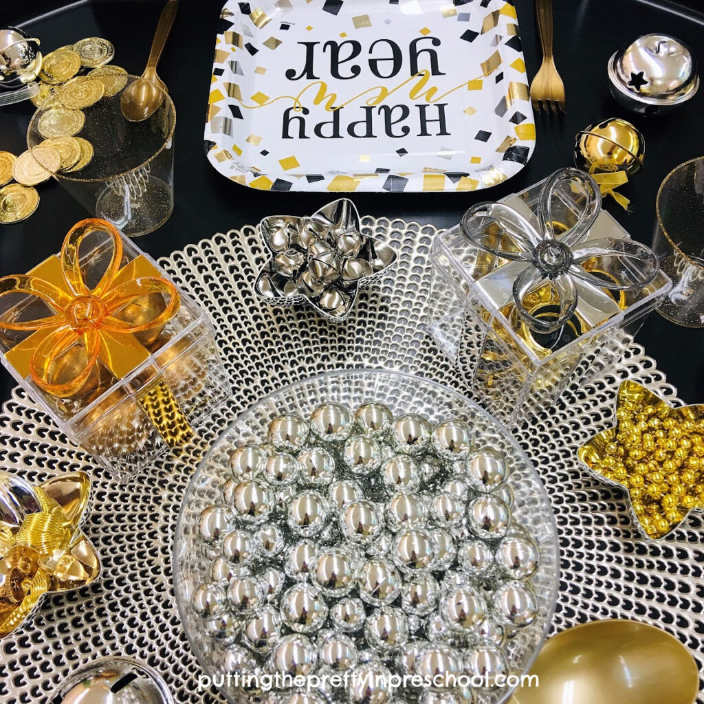 New Year's Eve sensory tray featuring dinnerware, gift boxes, and metallic loose parts.