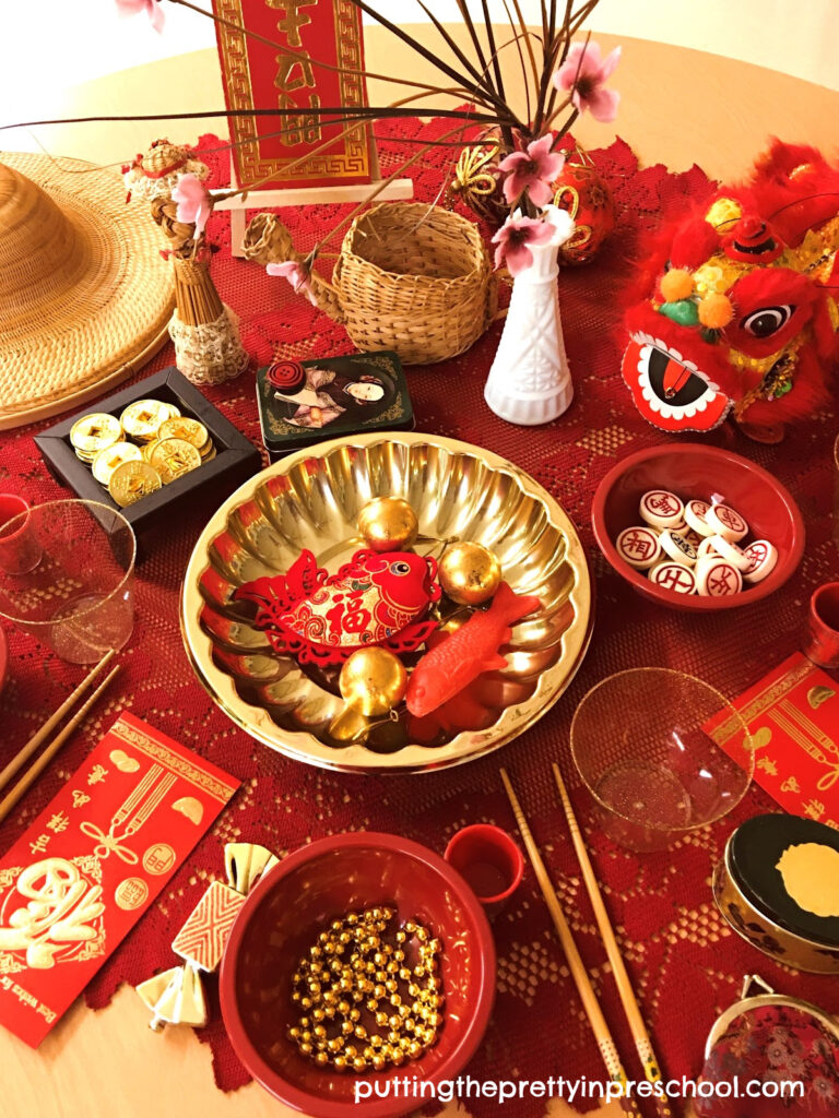 A Chinese New Year tablescape filled with Asian artifacts and red and gold loose parts for little learners to explore.