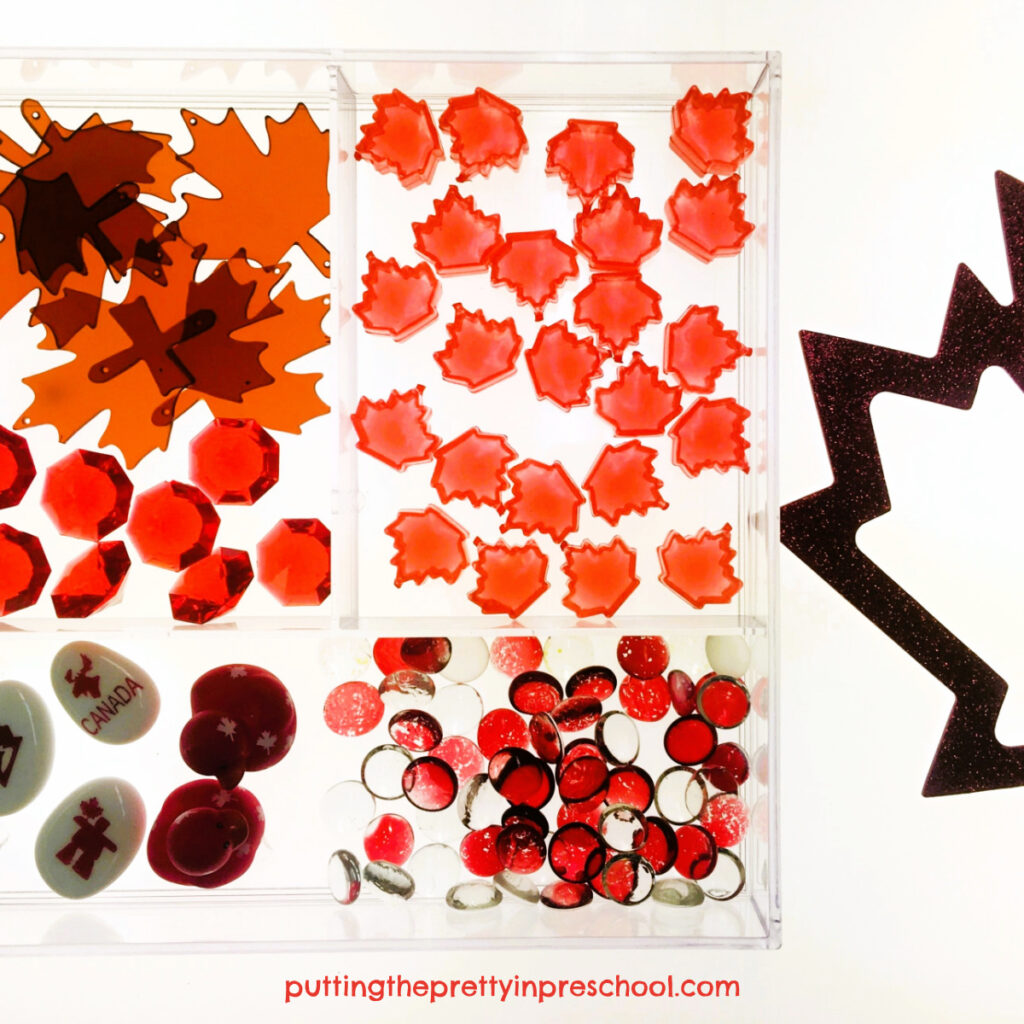 Transparent maple leaves and gems are gleaming loose parts in this Canada Day sensory invitation for the light table.