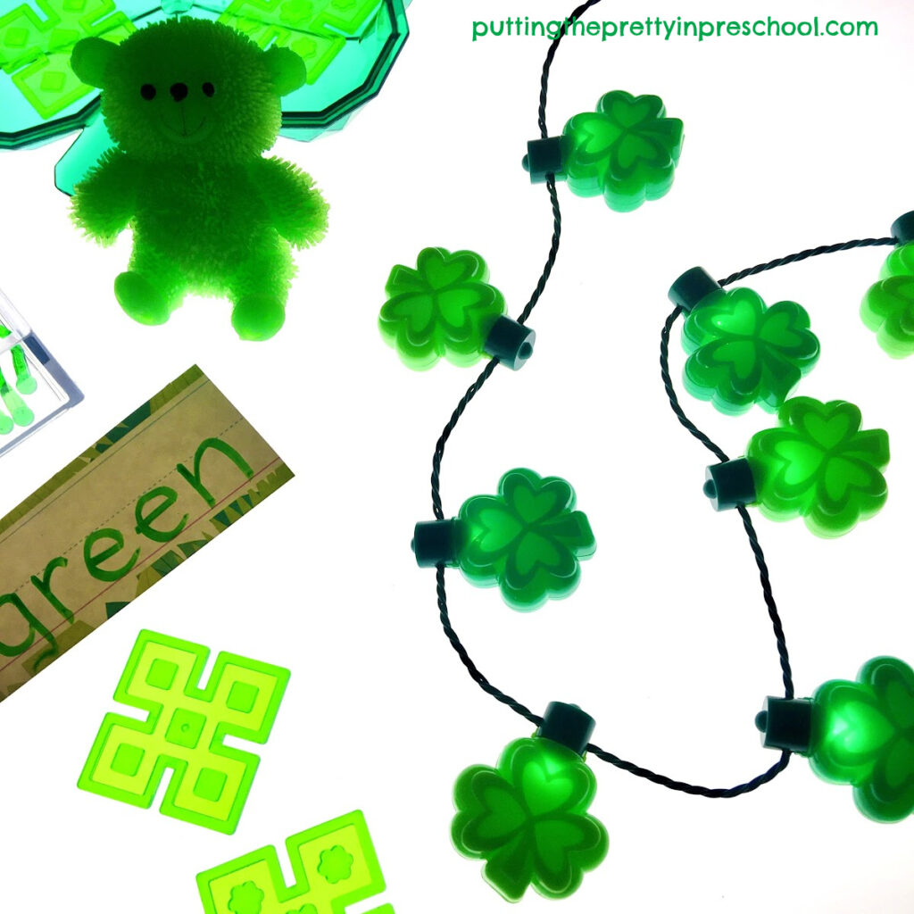A green shamrock light-up necklace is a highlight in a St. Patrick's Day light table center.