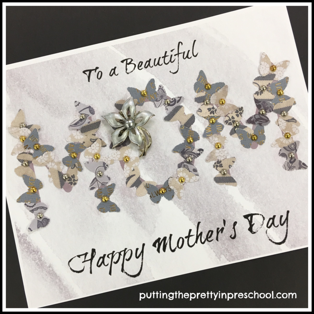 Mother's Day paper collage craft with butterflies glued on to the word "mom." A silver flower brooch is added on as a gift. This craft is suitable for all ages.