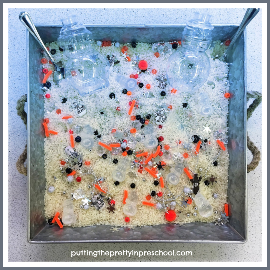 Snowman sensory tray with a rice base and loose parts. Snowman bottles, ice cubes, and buttons are the highlights of the tray.