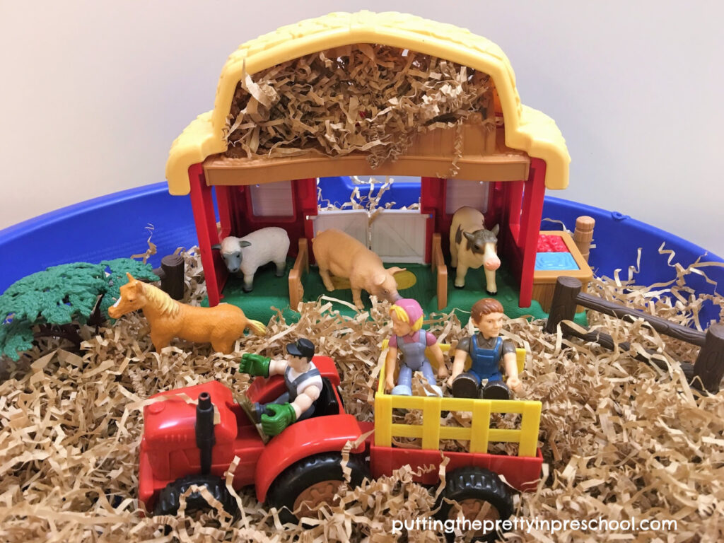 Haying time sensory bin with shredded paper hay, tractor, wagon, barnyard animals, and farm family figurines.