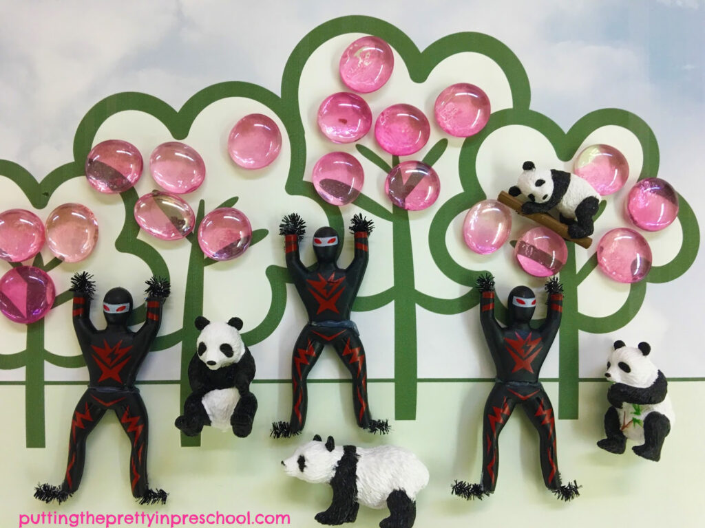 Tree placemat scene invitation to create with pink gems and ninja and panda bear figurines.