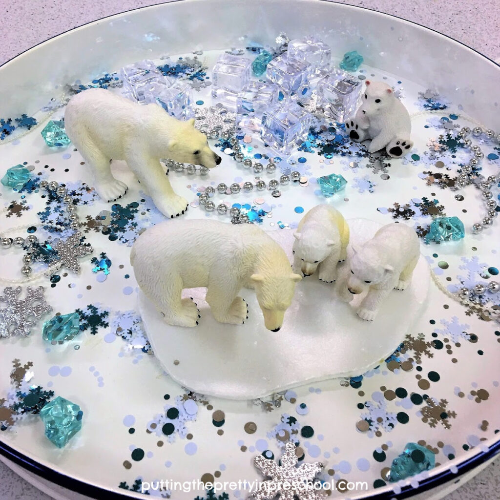 Polar bear winter sensory tray with a snowflake confetti base and shiny loose parts.