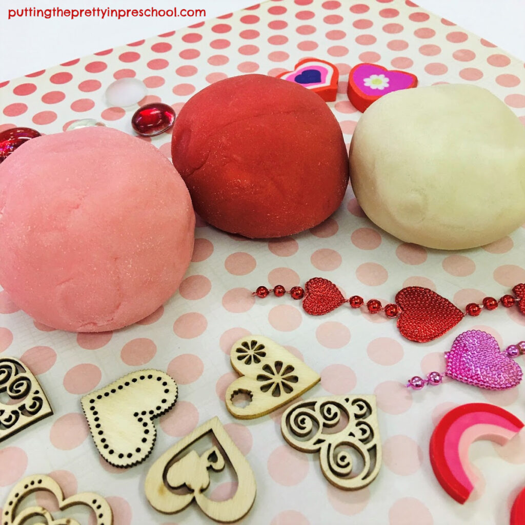 Valentine's Day playdough tray with loose parts and red, pink and white dough recipes.