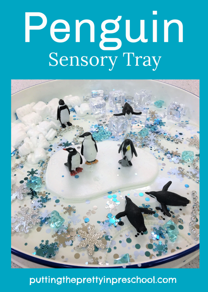 Penguin sensory tray with a winter-themed loose parts in a snowflake confetti base.
