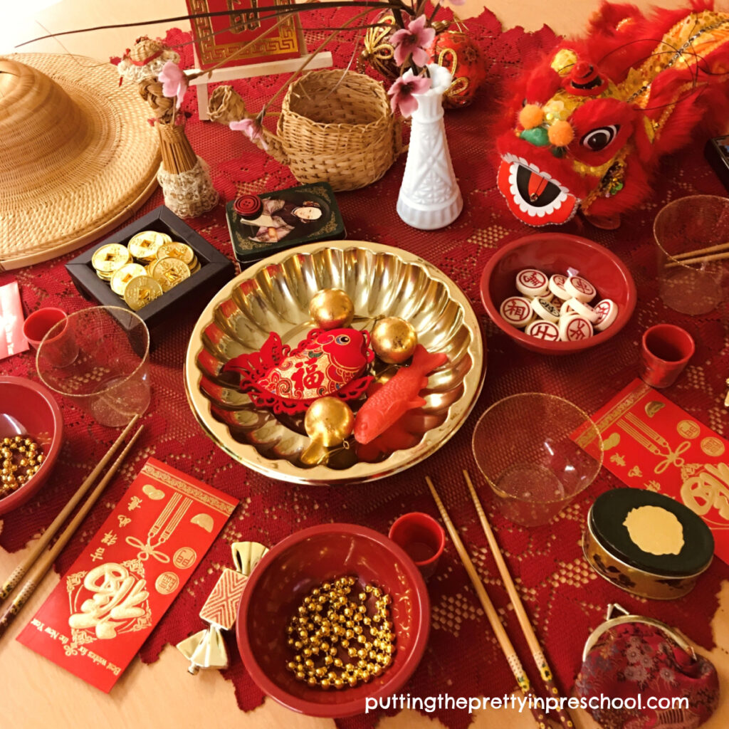 A Chinese New Year tablescape filled with Asian artifacts and red and gold loose parts for little learners to explore.