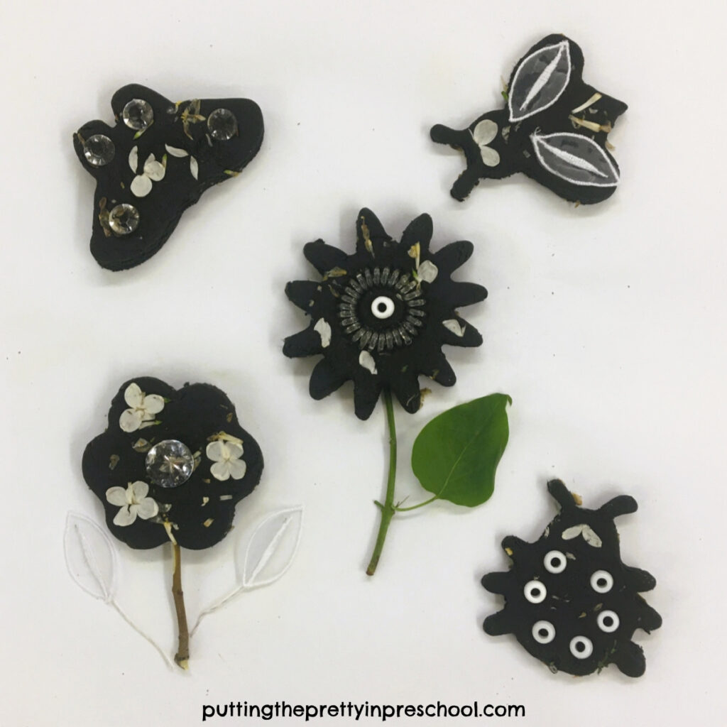 White lilac and black playdough creations using flower, butterfly, and bug coolie cutters and white and transparent loose parts.