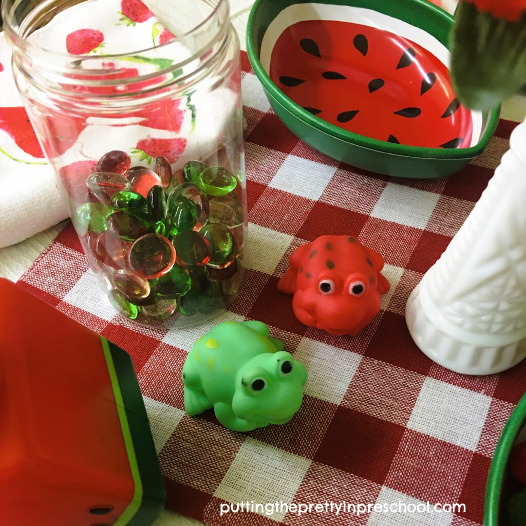 Rubber fogs and gem loose parts add interest and play possibilities to a watermelon dramatic play center.